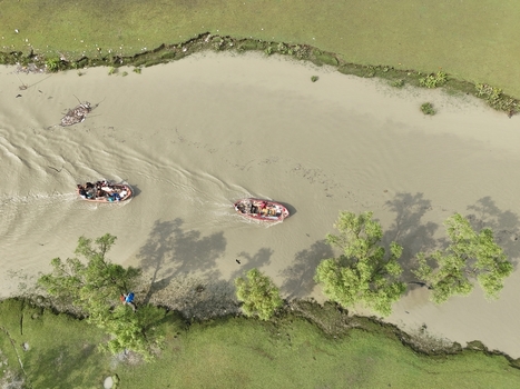 Aerial view of small boats carrying people along a river winding through lush green banks and trees in Sitakund Chittagong Division Bangladesh. Aerial view of small boats carrying people along a river winding through lush green banks and trees in Sitakund Chittagong Division Bangladesh.