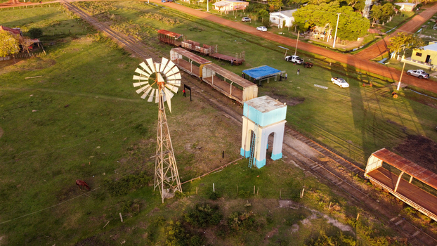 Aerial view of a rural landscape featuring a vintage windmill a blue and white water tower and old train cars resting on tracks in Guaviravi Corrientes Province Argentina. Aerial view of a rural landscape featuring a vintage windmill a blue and white water tower and old train cars resting on tracks in Guaviravi Corrientes Province Argentina.