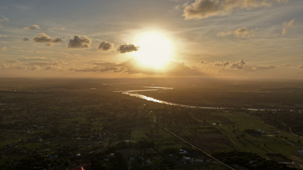 Aerial view of River Sabaki winding through the landscape during a golden sunset with soft clouds and lush fields in Malindi Kilifi County Kenya.