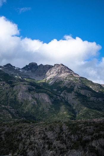 View of the rugged mountain peaks of the Andes with rocky slopes patches of green vegetation and a bright blue sky with white clouds in Futaleufu Chubut Argentina. View of the rugged mountain peaks of the Andes with rocky slopes patches of green vegetation and a bright blue sky with white clouds in Futaleufu Chubut Argentina.