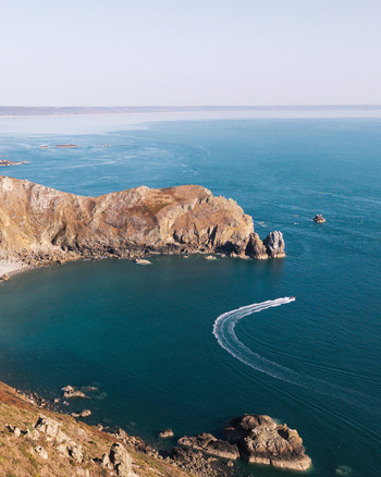 Aerial view of the rugged cliffs and deep blue sea with a small boat leaving a white wake in the water La Hague Normandie France. Aerial view of the rugged cliffs and deep blue sea with a small boat leaving a white wake in the water La Hague Normandie France.