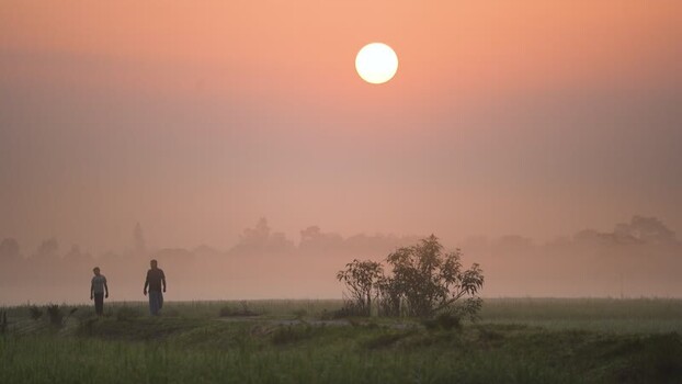 View of two people walking in a misty field at sunrise Bangladesh View of two people walking in a misty field at sunrise Bangladesh
