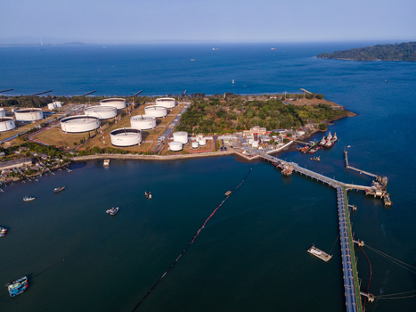 Aerial view of an oil terminal with large storage tanks a long jetty extending into the sea and small boats near the coast in Cilacap Regency Central Java Indonesia. Aerial view of an oil terminal with large storage tanks a long jetty extending into the sea and small boats near the coast in Cilacap Regency Central Java Indonesia.