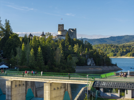 Aerial view of Niedzica Castle overlooking the Czorsztyn Reservoir with a pedestrian bridge in the foreground lush green trees and blue sky in Niedzica Wojewodztwo malopolskie Poland.