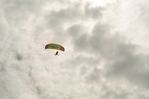 View of a powered paraglider with a colorful wing soaring through a dense layer of grey overcast clouds in Sri Lanka. View of a powered paraglider with a colorful wing soaring through a dense layer of grey overcast clouds in Sri Lanka.