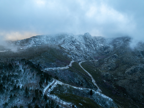 Aerial view of the snow covered Serra da Estrela mountain range with a winding road and low clouds in Unhais da Serra Castelo Branco District Portugal. Aerial view of the snow covered Serra da Estrela mountain range with a winding road and low clouds in Unhais da Serra Castelo Branco District Portugal.