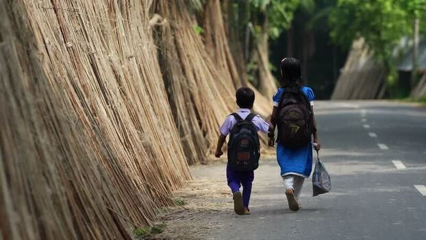 View of school children walking past dried jute stalks Bangladesh.