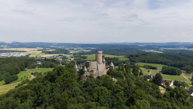 Aerial view of Nurburg Castle perched on a forested hill surrounded by lush green fields and rolling hills in the Eifel region Nurburg Rhineland Palatinate Germany. Aerial view of Nurburg Castle perched on a forested hill surrounded by lush green fields and rolling hills in the Eifel region Nurburg Rhineland Palatinate Germany.