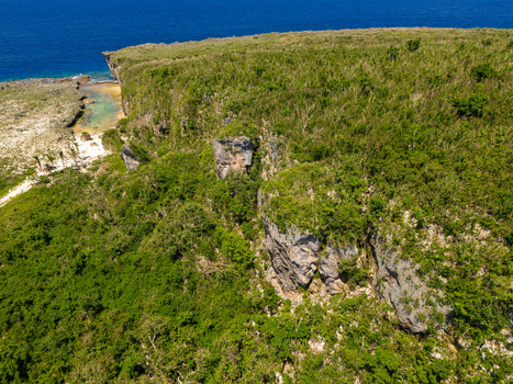 Aerial view of Chigit Beach featuring rugged limestone cliffs and lush tropical vegetation overlooking the turquoise Pacific Ocean in Northern Tinian Tinian Northern Mariana Islands. Aerial view of Chigit Beach featuring rugged limestone cliffs and lush tropical vegetation overlooking the turquoise Pacific Ocean in Northern Tinian Tinian Northern Mariana Islands.
