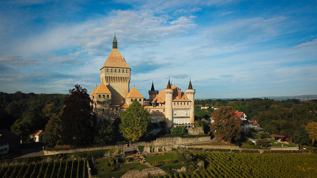 Aerial view of the medieval Vufflens Castle with its prominent square keep and turrets surrounded by lush vineyards and green trees under a blue sky in Vufflens le Chateau Vaud Switzerland. Aerial view of the medieval Vufflens Castle with its prominent square keep and turrets surrounded by lush vineyards and green trees under a blue sky in Vufflens le Chateau Vaud Switzerland.