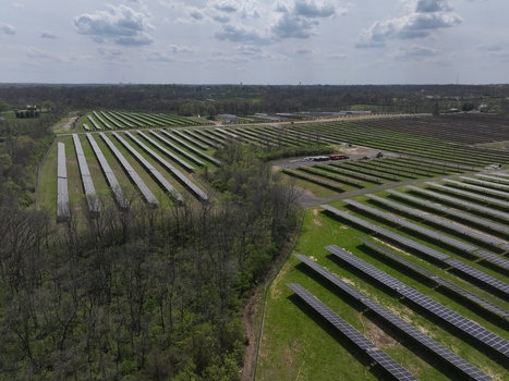 Lebanon United States 12 April 2026 Aerial view of a large solar farm with rows of photovoltaic panels surrounded by green fields and dense woodland under a cloudy sky.