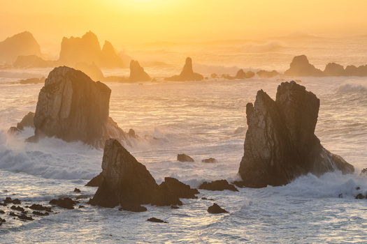 View of Silence Beach featuring jagged rock formations and crashing waves under a misty golden sunset in Asturias Asturias Spain.