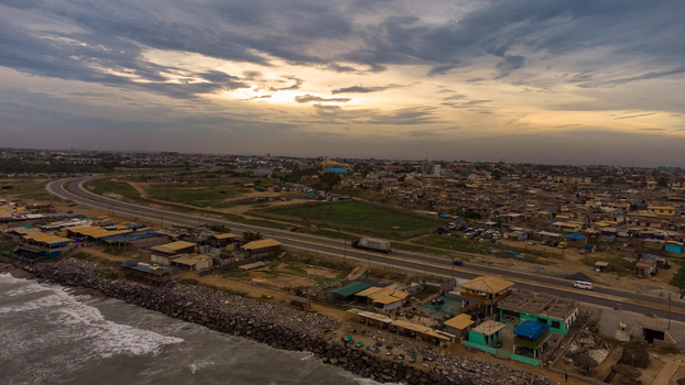 Aerial view of Accra Tema Beach Road stretching along the coastline with nearby buildings rocky shoreline and a cloudy sunset sky in Accra Greater Accra Region Ghana.