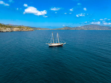 Aerial view of a sailboat sailing on the deep blue sea near the coast of Lacona Tuscany Italy.