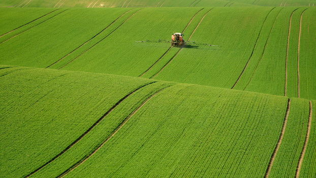 View of a tractor spraying a large rolling green field in the Moravia region Brno City District South Moravian Region Czechia.