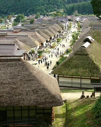 View of Ouchi juku with traditional thatched roof houses lining the main street and visitors walking along the path in Shimogo Fukushima Japan.