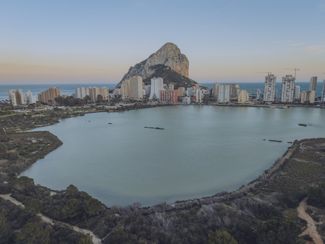 Aerial view of the Penon de Ifach rising above the coastal city of Calp with high rise buildings and the calm waters of Las Salinas salt lake. Calp Valencian Community Spain. Aerial view of the Penon de Ifach rising above the coastal city of Calp with high rise buildings and the calm waters of Las Salinas salt lake. Calp Valencian Community Spain.