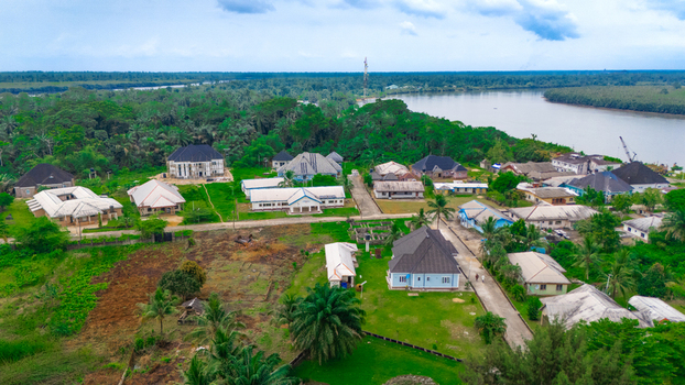 Aerial view of a rural settlement with scattered houses lush tropical vegetation and palm trees situated along a riverbank in Minima Rivers Nigeria.