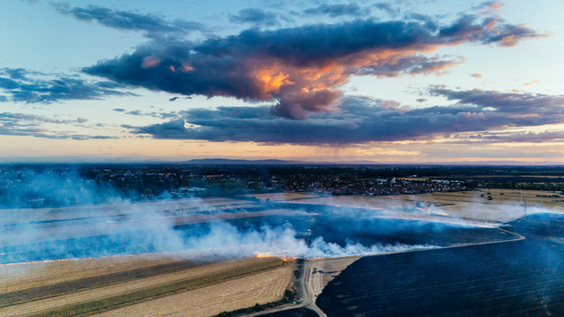Aerial view of a controlled field fire burning across agricultural land at sunset with smoke rising under a dramatic cloudy sky near Sremska Mitrovica Vojvodina Serbia. Aerial view of a controlled field fire burning across agricultural land at sunset with smoke rising under a dramatic cloudy sky near Sremska Mitrovica Vojvodina Serbia.