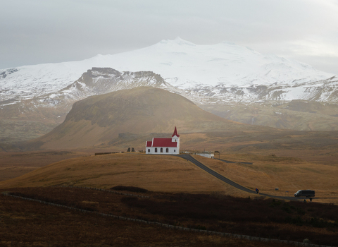 Aerial view of Ingjaldsholl Church with its red roof set against snow capped mountains and rugged terrain in the Icelandic countryside. Hellissandur Snaefellsbaer Iceland. Aerial view of Ingjaldsholl Church with its red roof set against snow capped mountains and rugged terrain in the Icelandic countryside. Hellissandur Snaefellsbaer Iceland.