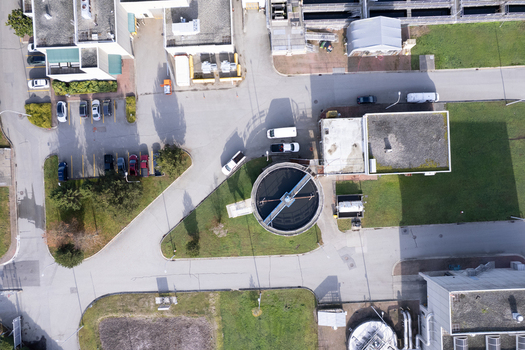 Aerial view of the wastewater treatment plant featuring a large circular clarifier tank industrial buildings and surrounding parking areas in Richmond British Columbia Canada. Aerial view of the wastewater treatment plant featuring a large circular clarifier tank industrial buildings and surrounding parking areas in Richmond British Columbia Canada.
