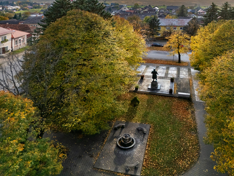Aerial view of a serene autumnal park where golden and green foliage frames a solemn statue and a dark modern fountain Mosovce Zilina Region Slovakia. Aerial view of a serene autumnal park where golden and green foliage frames a solemn statue and a dark modern fountain Mosovce Zilina Region Slovakia.