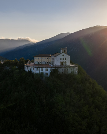 Aerial view of the Santuario del Santissimo Salvatore perched on a forested hilltop with sun rays over the mountains in Montella Campania Italy. Aerial view of the Santuario del Santissimo Salvatore perched on a forested hilltop with sun rays over the mountains in Montella Campania Italy.