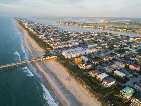 Aerial view of Wrightsville Beach featuring a pier coastal homes and sandy shoreline under golden hour light in Wrightsville Beach North Carolina United States.