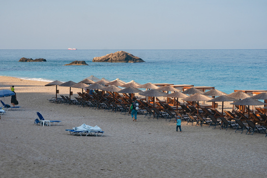 View of endless rows of straw umbrellas and beach chairs line the golden sands meeting the turquoise sea under a clear sky Lefkada Greece. View of endless rows of straw umbrellas and beach chairs line the golden sands meeting the turquoise sea under a clear sky Lefkada Greece.