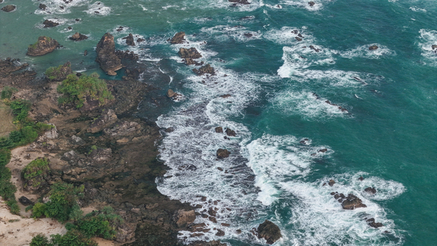 Aerial view of the rocky coastline with turquoise water and crashing waves along the shore in Indonesia. Aerial view of the rocky coastline with turquoise water and crashing waves along the shore in Indonesia.