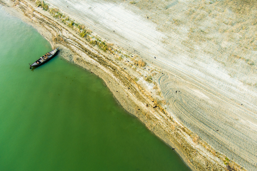 Aerial view of a traditional wooden boat moored on the sandy riverbank of the Padma River with birds flying over the shore in Rajshahi Rajshahi Division Bangladesh.