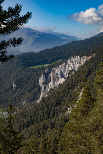 View of the Swiss Alps near Airolo featuring rugged rocky cliffs dense pine forests and a lush green valley under a blue sky in Airolo Ticino Switzerland. View of the Swiss Alps near Airolo featuring rugged rocky cliffs dense pine forests and a lush green valley under a blue sky in Airolo Ticino Switzerland.