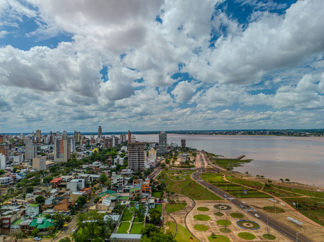 Aerial view of the Posadas skyline featuring high rise buildings and a riverfront park along the Parana River under a cloudy sky in Posadas Misiones Province Argentina.