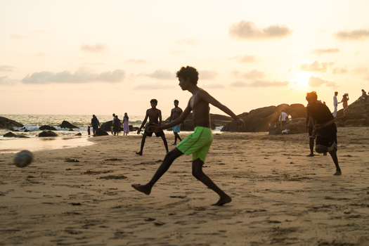 Sri Lanka 25 January 2026 View of young men playing football on a sandy beach during a golden sunset with silhouettes against the ocean and rocky shore.