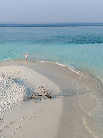 Aerial view of a lone figure standing on a pristine sandbar where turquoise waters meet the shore Dhidhdhoo Thiladhunmathi Atoll Maldives.