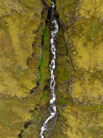 Aerial view of a narrow stream flowing through a deep moss covered canyon with rugged rock formations in the Eastern Region Iceland. Aerial view of a narrow stream flowing through a deep moss covered canyon with rugged rock formations in the Eastern Region Iceland.