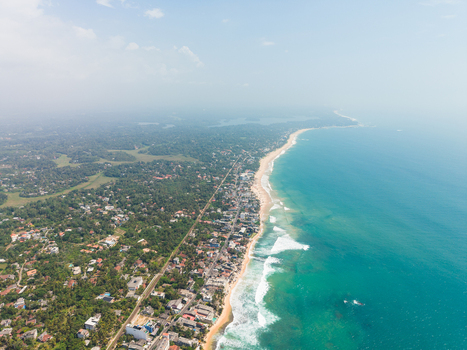Aerial view of the sandy coastline and turquoise ocean waves bordering the coastal town with lush tropical greenery Hikkaduwa Southern Province Sri Lanka. Aerial view of the sandy coastline and turquoise ocean waves bordering the coastal town with lush tropical greenery Hikkaduwa Southern Province Sri Lanka.
