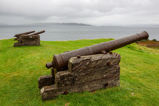 View of historic iron cannons at Duart Castle overlooking the sea under a cloudy sky from a grassy hill Isle of Mull Scotland United Kingdom.