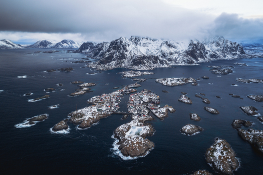 Aerial view of snow dusted islands scattered across the dark moody sea with the village of Henningsv&aelig;r nestled amidst the stark snow capped mountains Henningsv&aelig;r Nordland Norway.