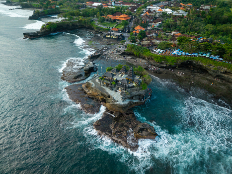 Aerial view of Tanah Lot Temple situated on a rocky outcrop surrounded by crashing waves and lush coastal greenery in Kecamatan Kediri Bali Indonesia. Aerial view of Tanah Lot Temple situated on a rocky outcrop surrounded by crashing waves and lush coastal greenery in Kecamatan Kediri Bali Indonesia.