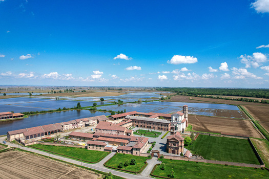 Aerial view of the historic Abbazia di Lucedio complex surrounded by flooded rice fields and green meadows under a clear blue sky in Trino Piemonte Italy.