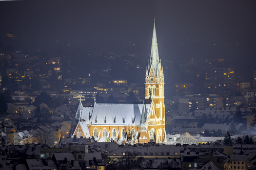 View of the brightly lit Herz Jesu church standing majestically against the dark sky its spire piercing the night above the city Graz Styria Austria. View of the brightly lit Herz Jesu church standing majestically against the dark sky its spire piercing the night above the city Graz Styria Austria.