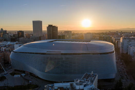Aerial view of Santiago Bernabeu stadium featuring its modern metallic facade during sunset with the Madrid skyline in the background Madrid Community of Madrid Spain. Aerial view of Santiago Bernabeu stadium featuring its modern metallic facade during sunset with the Madrid skyline in the background Madrid Community of Madrid Spain.
