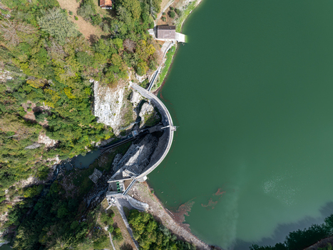 Aerial view of Barrage de Montsalvens a curved concrete dam holding back a deep green reservoir surrounded by forest and rocky cliffs in Chatel sur Montsalvens Fribourg Switzerland. Aerial view of Barrage de Montsalvens a curved concrete dam holding back a deep green reservoir surrounded by forest and rocky cliffs in Chatel sur Montsalvens Fribourg Switzerland.