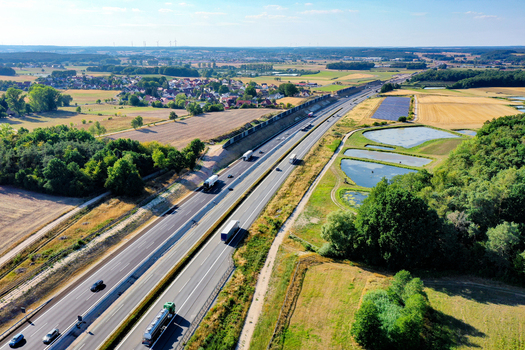 Aerial view of a busy highway with trucks and cars driving through rural landscapes green fields and a small village under a clear blue sky Hochstadt Bavaria Germany. Aerial view of a busy highway with trucks and cars driving through rural landscapes green fields and a small village under a clear blue sky Hochstadt Bavaria Germany.