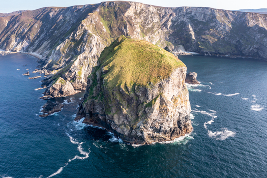 Aerial view of Glenlough Bay featuring a prominent sea stack rising from the Atlantic Ocean surrounded by rugged cliffs and deep blue water in Ardara County Donegal Ireland.