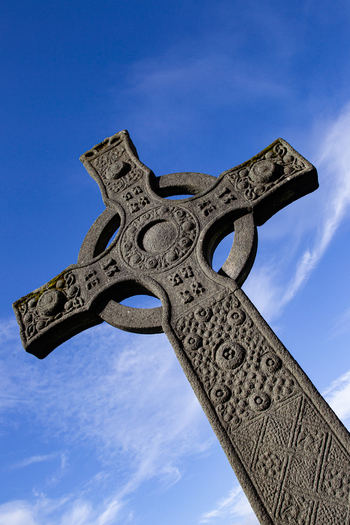 View of the intricate carvings on a historic stone Celtic cross at Iona Abbey under a bright blue sky Isle of Iona Scotland United Kingdom. View of the intricate carvings on a historic stone Celtic cross at Iona Abbey under a bright blue sky Isle of Iona Scotland United Kingdom.