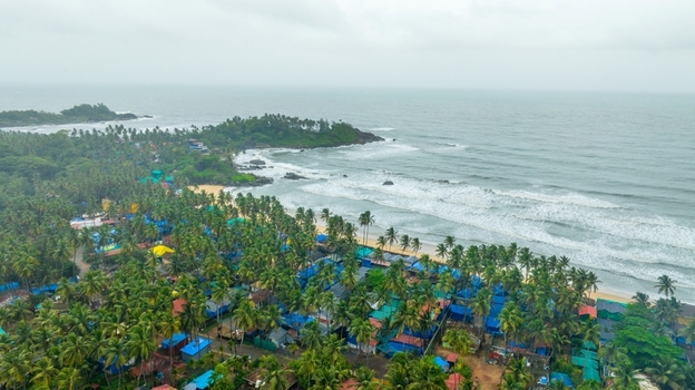 Aerial view of Palolem Beach with lush palm trees colorful beach huts and waves crashing on the sandy shore in Canacona Goa India.