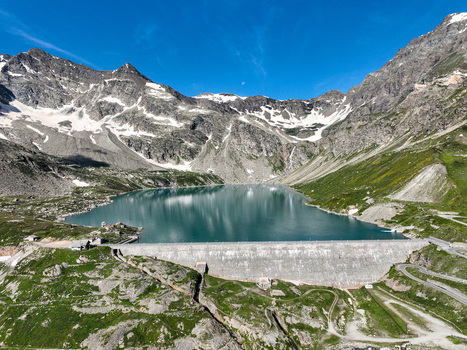 Aerial view of Serru Lake and its massive dam surrounded by rugged alpine peaks with snow patches and winding mountain roads in Ceresole Reale Piedmont Italy. Aerial view of Serru Lake and its massive dam surrounded by rugged alpine peaks with snow patches and winding mountain roads in Ceresole Reale Piedmont Italy.