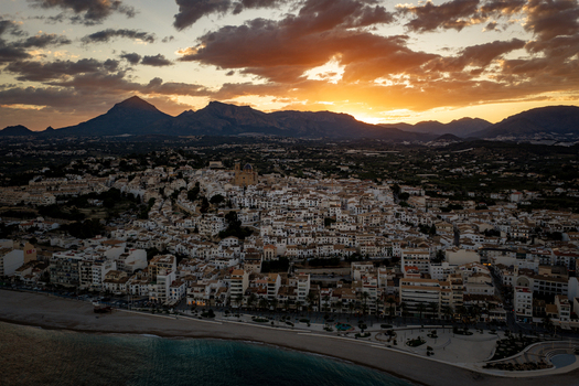 Aerial view of the historic town of Altea with its white buildings and iconic church dome nestled against the mountains under a dramatic sunset sky in Altea Valencian Community Spain.